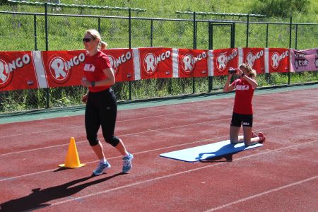 Laufanalyse mit RUNNING Company: Eine Läuferin läuft auf einer roten Laufbahn und wird dabei von einer hinter ihr knieenden Person mit einer Videokamer gefilmt.